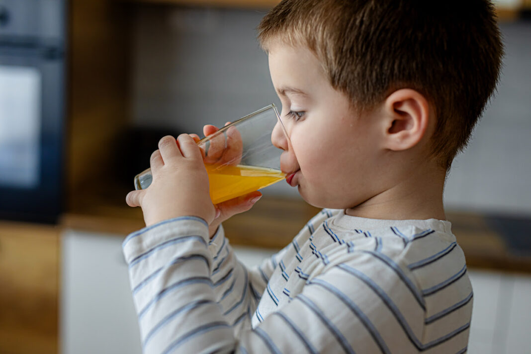 A young child drinks juice in a modern kitchen filled with soft natural light